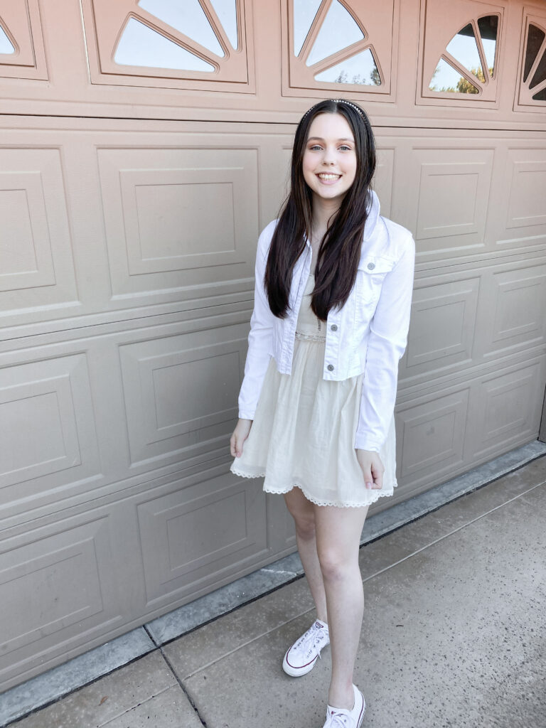 feminine fashion blogger wearing all white monochromatic outfit with white crochet dress, white jean jacket, white pearl headband, white pearl heart earrings, white low top converse, and white pearl bracelet