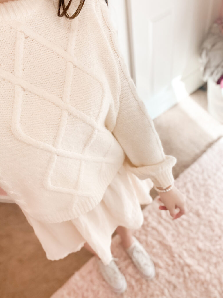 fashion blogger wearing all white monochromatic outfit with white crochet dress , white puff sleeve sweater with cable knit design, white low top converse, and white pearl bracelet